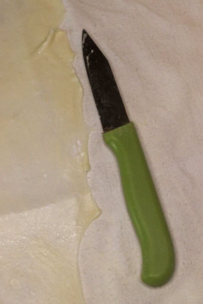 Cutting the edges of homemade strudel phyllo dough using a small knife. 