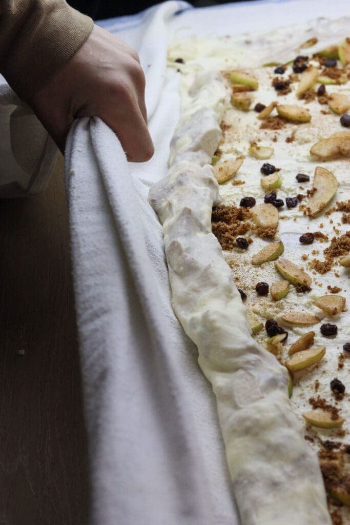 Freshly made pear strudel with cottage cheese and raisins being rolled up into  a large strudel log. 