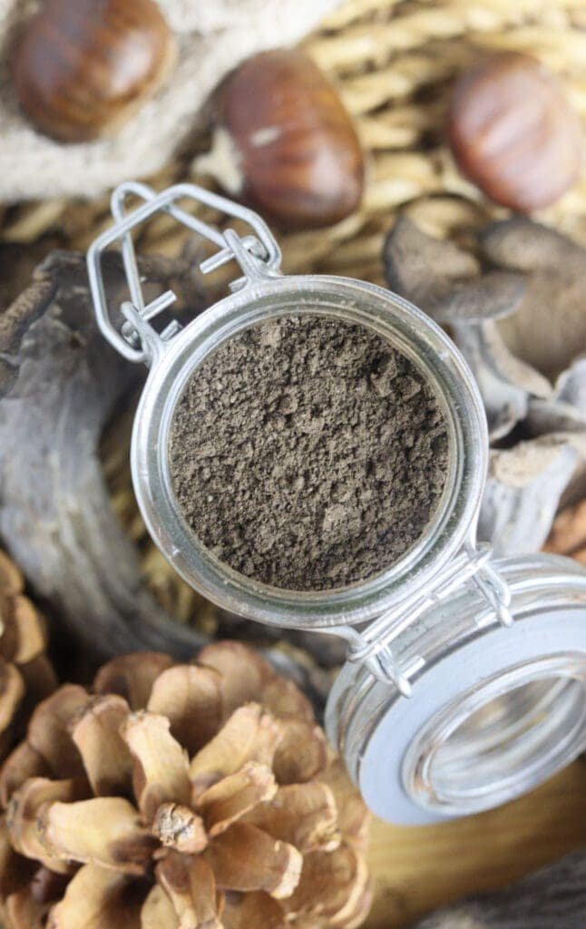 a close top view of an open jar filled with black trumpet mushroom powder with chestnuts in the bacground