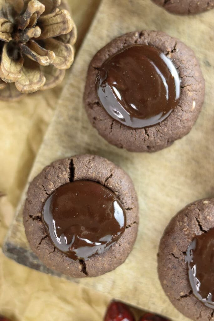 Three buckwheat chocolate thumbprint cookies on a wooden plate, looking delicious and ready to be eaten.