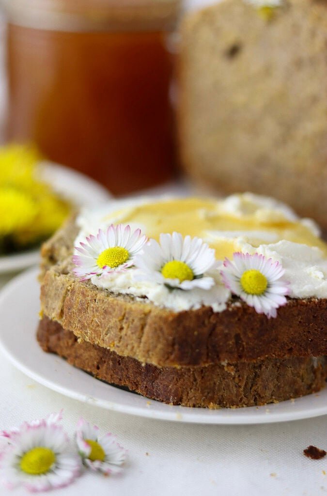A piece of dandelion bread made with buckwheat flour with cream cheese and honey on top and three daisies for decoration. 