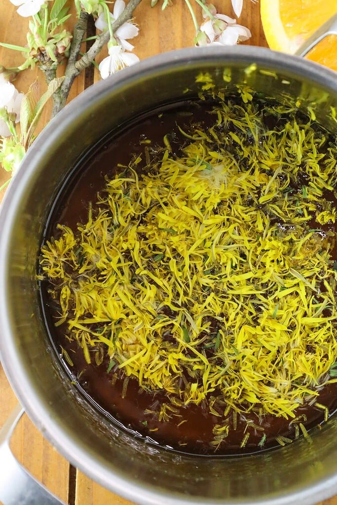 Dandelion flower petals mixed into hot apricot jam in a saucepan. 