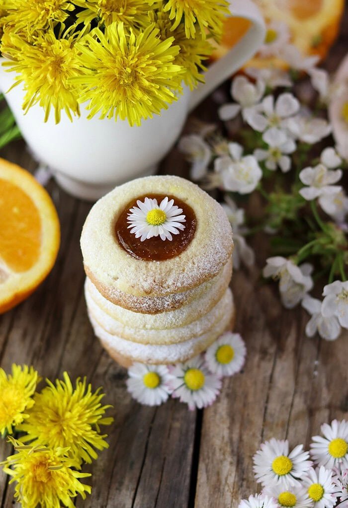 A top view of a stack of dandelion thumbprint cookies with a vase full of dandelions in the background.
