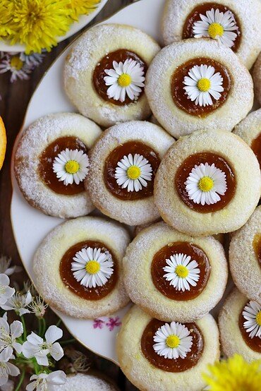 Dandelion thumbprint cookies with flowers on a white plate with dandelion petals in the background.