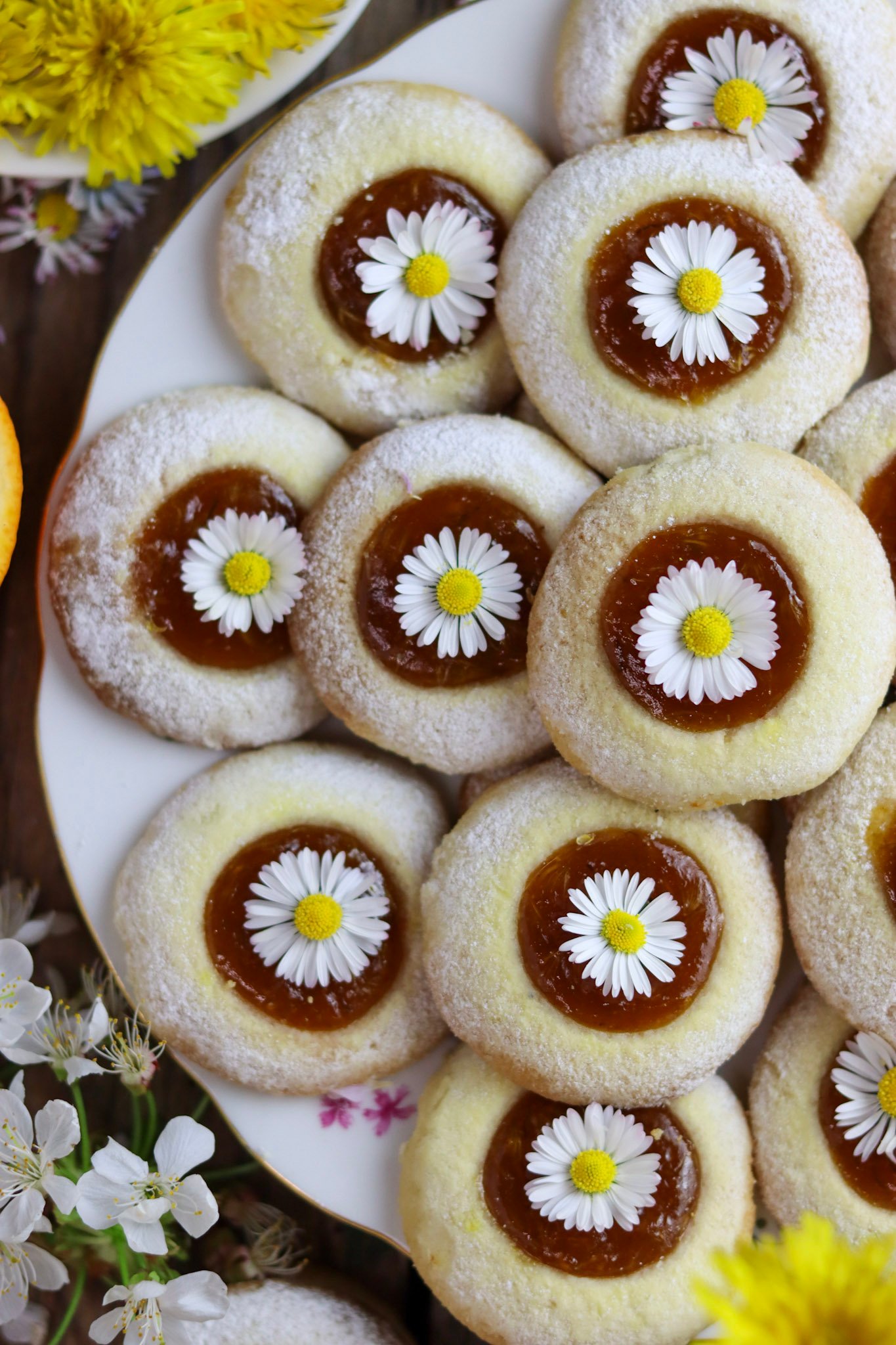 Dandelion thumbprint cookies with flowers on a white plate with dandelion petals in the background.