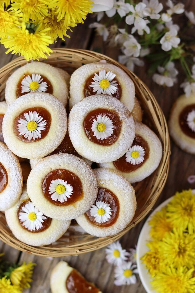 A basket of homemade dandelion cookies filled with apricot jam with blurred flowers in the background.
