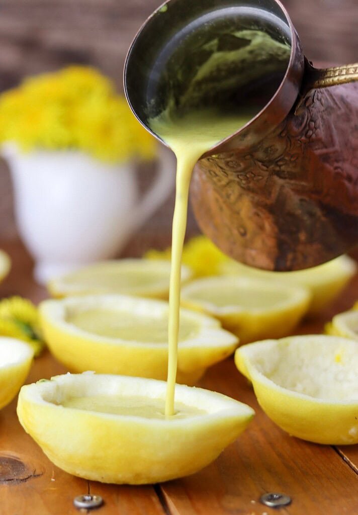 Process shot – pouring the filling Pouring dandelion lemon posset cream into hollowed lemon shells on a wooden surface, ready to set into a dandelion dessert.
