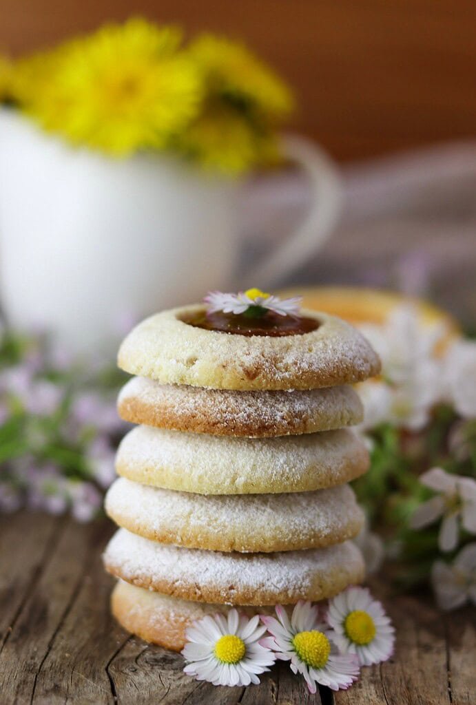 A close view of a stack of dandelion cookies, decorated with flowers and dandelion bouqet in the background.
