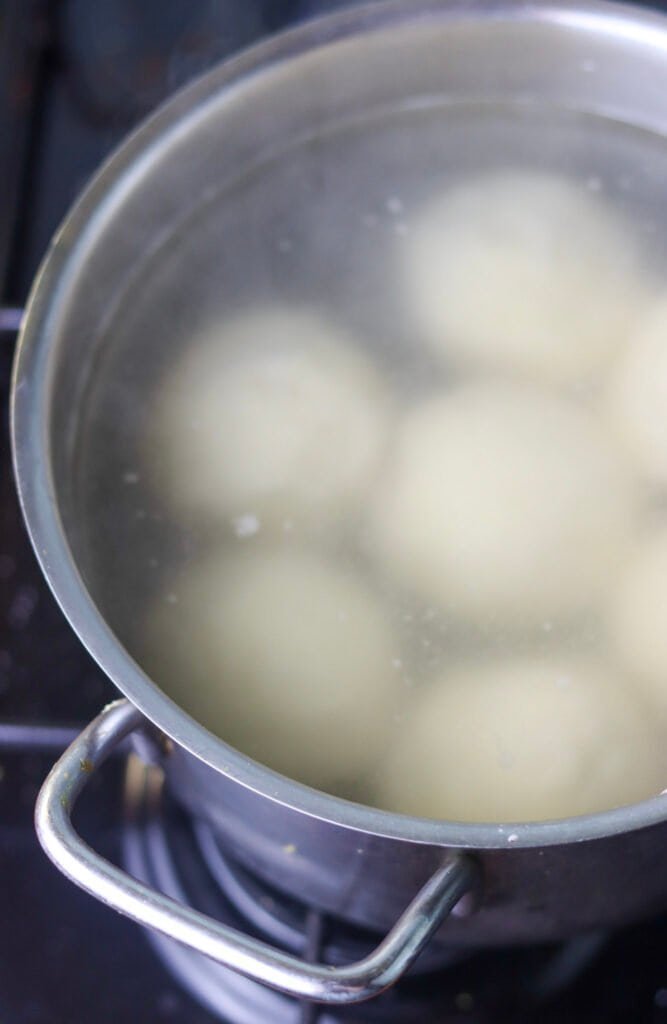 Plum dumplings being cooked in boiling water, in a pot on the gas cooker.