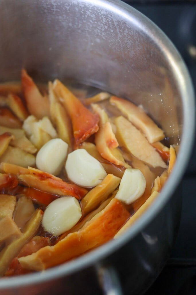 Chicken of the woods slices boiling in a pot with vinegar, white wine and garlic cloves.