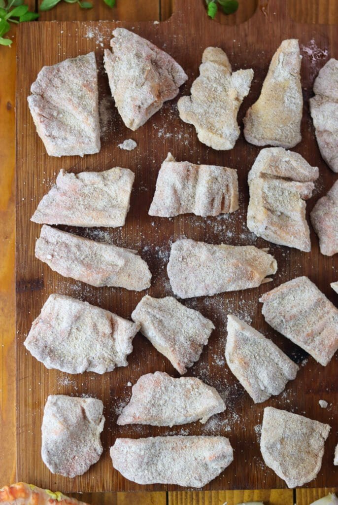 Pieces of chicken of the woods mushroom slices, floured and spiced, on a wooden cutting board.