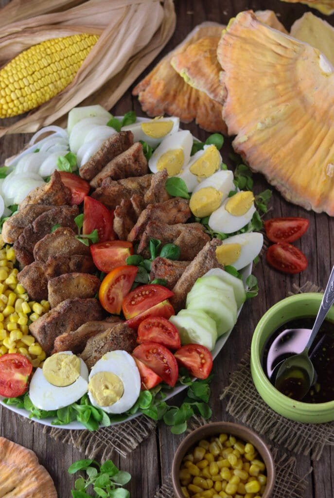 A plate of fried chicken of the woods mushroom salad with corn, vinegar and fresh mushroom in the bacground.