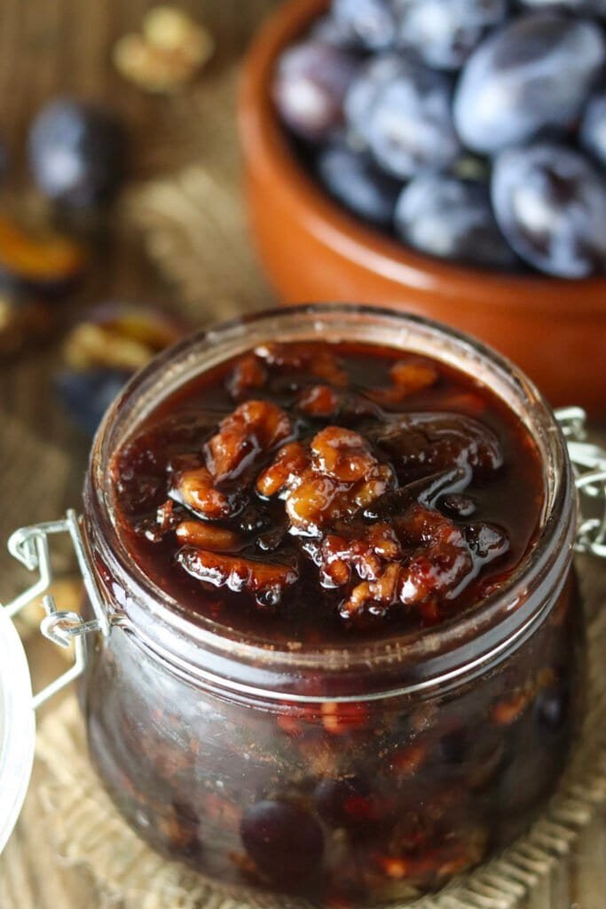 An opened jar of honey preserve with plums and walnuts on the table.