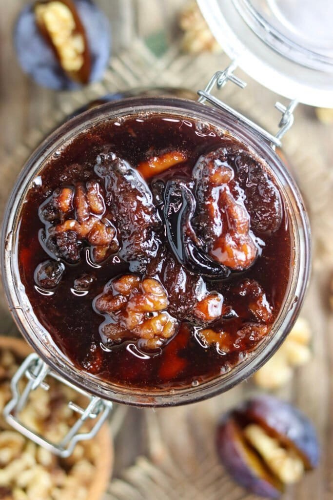 Top view of an opened jar, filled with plum preserve with honey and walnuts.