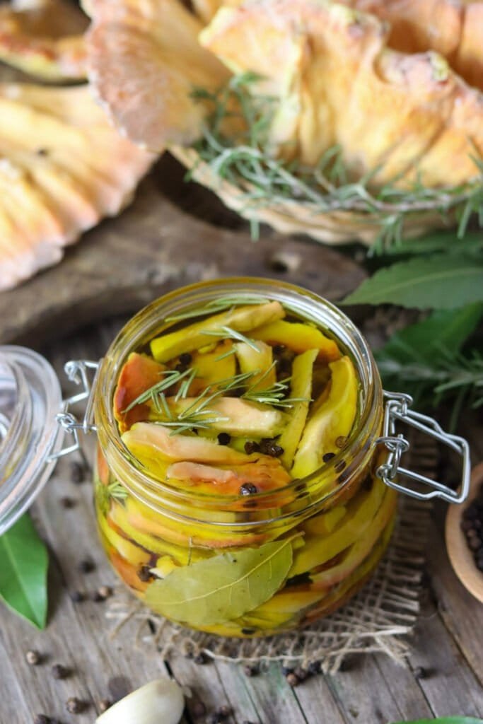 An opened jar of pickled chicken of the woods mushroom on a rustic table.