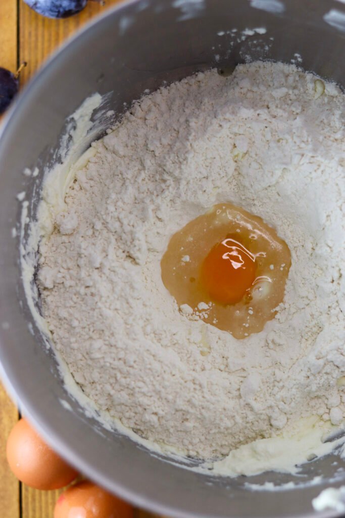 Mixing flour, an egg, butter, cottage cheese and salt into delicious quick plum dumpling dough.