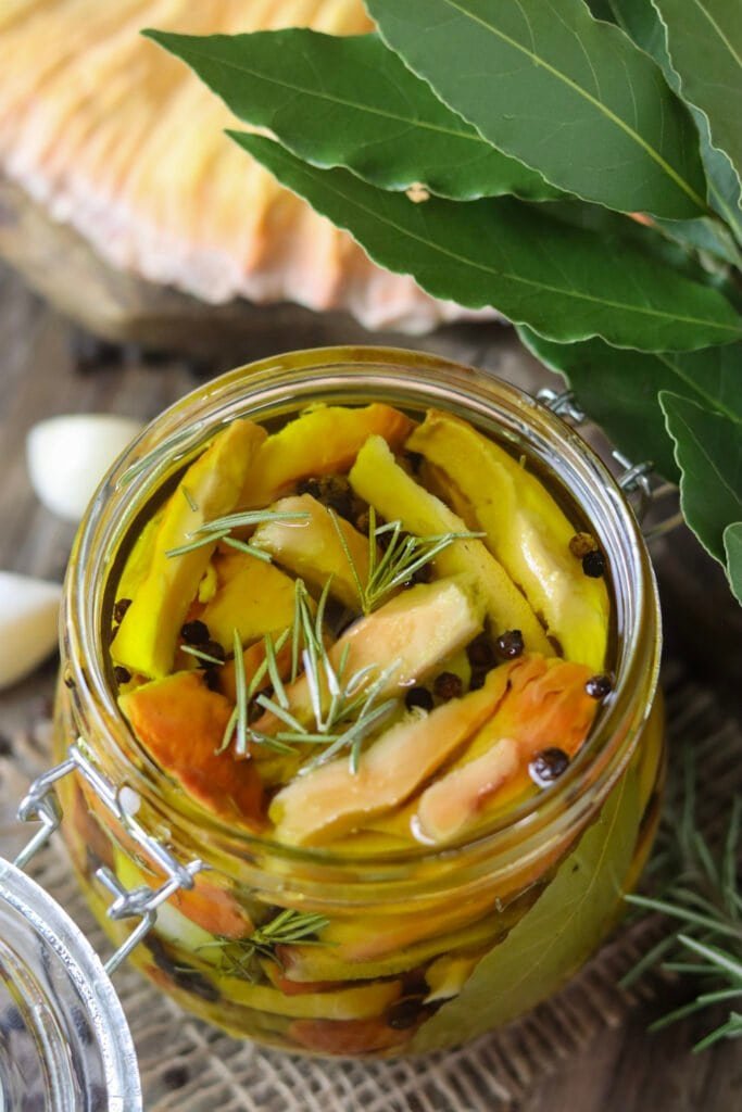 A jar of pickled chicken of the woods in olive oil, with fresh chicken of the woods in the background.