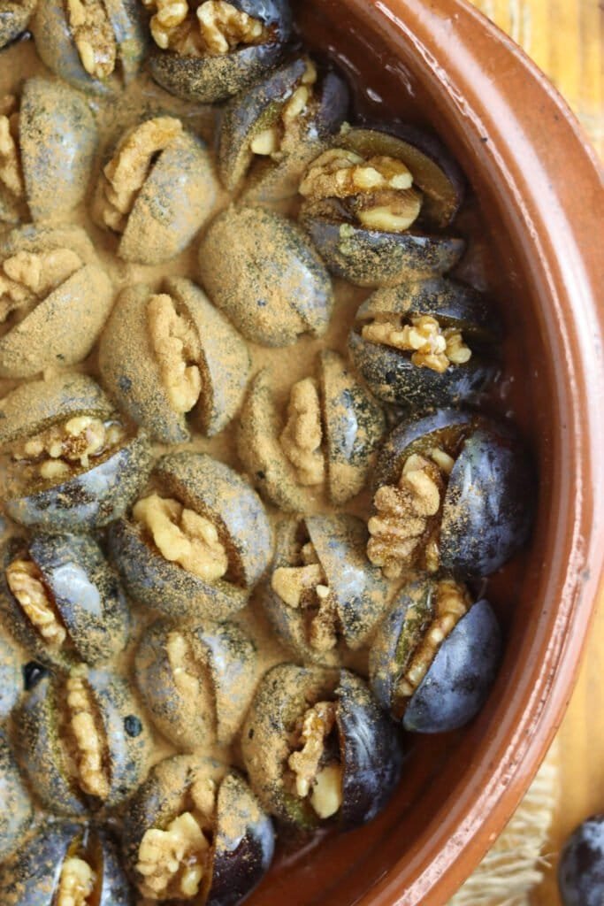 Plums stuffed with walnuts in a baking pot, covered with honey and cinnamon, ready to be baked.