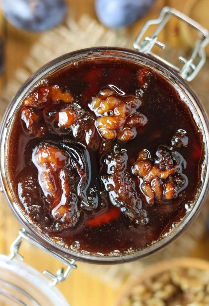 Top view of plums with walnuts in a jar, covered with honey plum sauce.