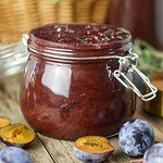 Plum jam with canned jars and fresh, ripe plums in the background.