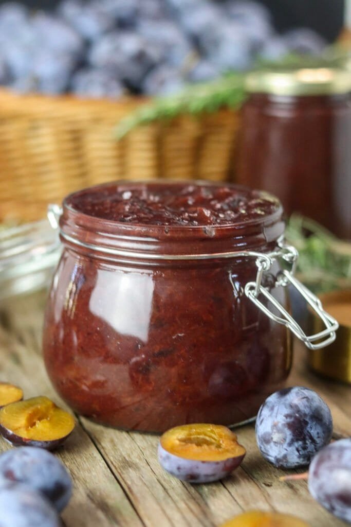 Plum jam with canned jars and fresh, ripe plums in the background.