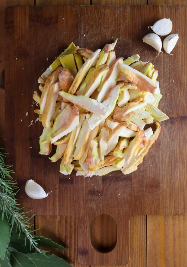 Sliced chicken of the woods mushroom on a wooden cutting board with garlic cloves.
