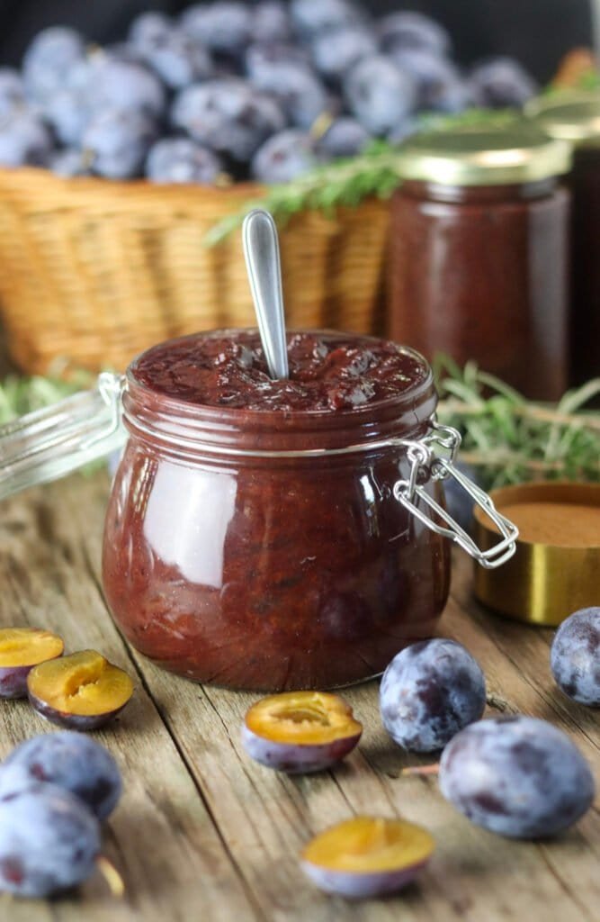 An open jar of sugar free plum jam with cinnamon, with fresh plums and canned jars of jam in the background.
