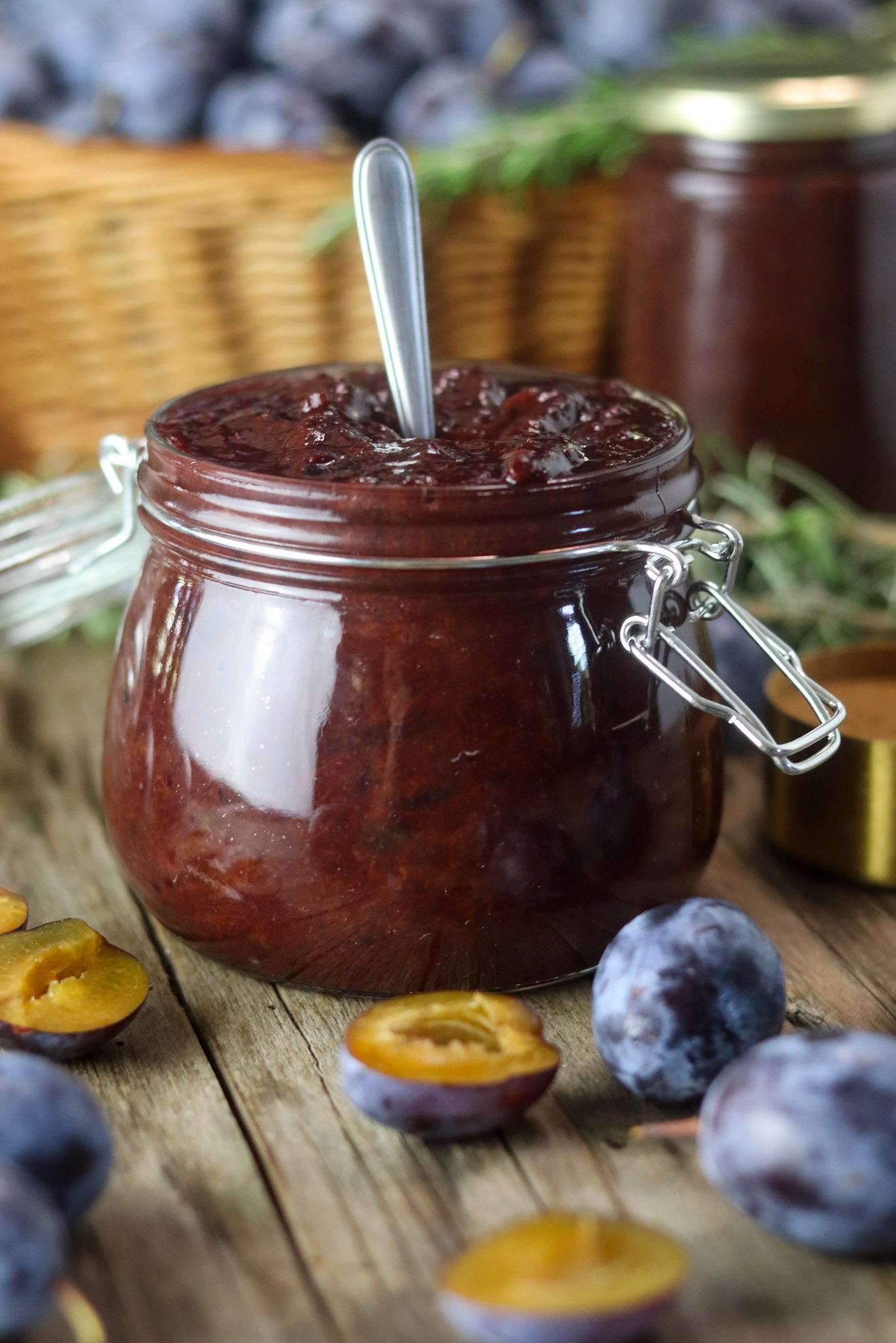A full jar of sugar free plum jam with cinnamon, with fresh plums and a jar of canned plum jam with basket full of plums in the background.