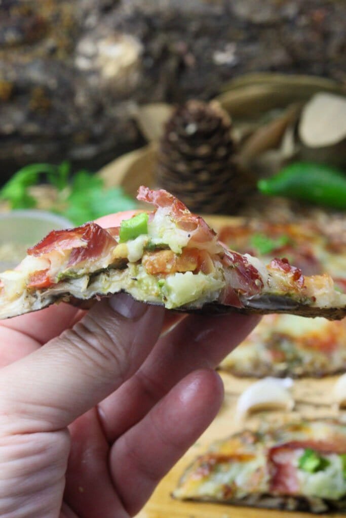 My hand holding a slice of parasol mushroom pizza with more pizza slices in the background.