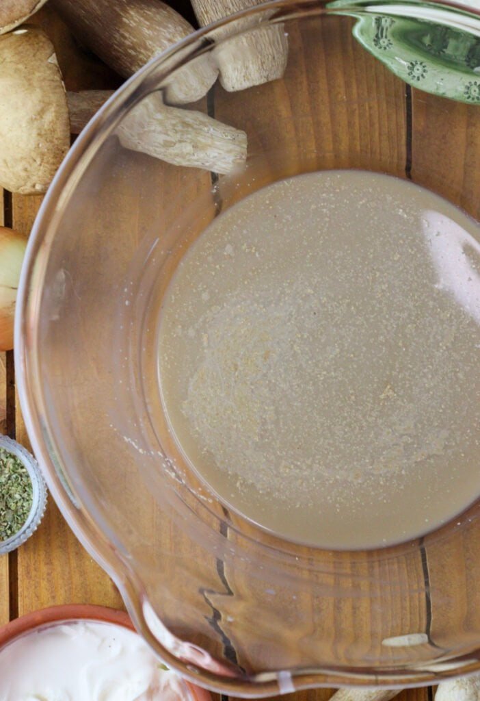 A glass bowl with dry yeast, warm water and a teaspoon of sugar.