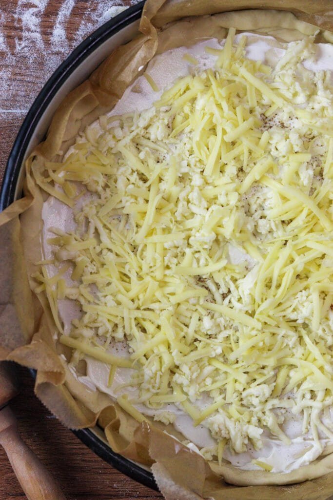 Adding mozzarella and cheddar to the pizza dough, on top of white sauce with cream cheese and sour cream.