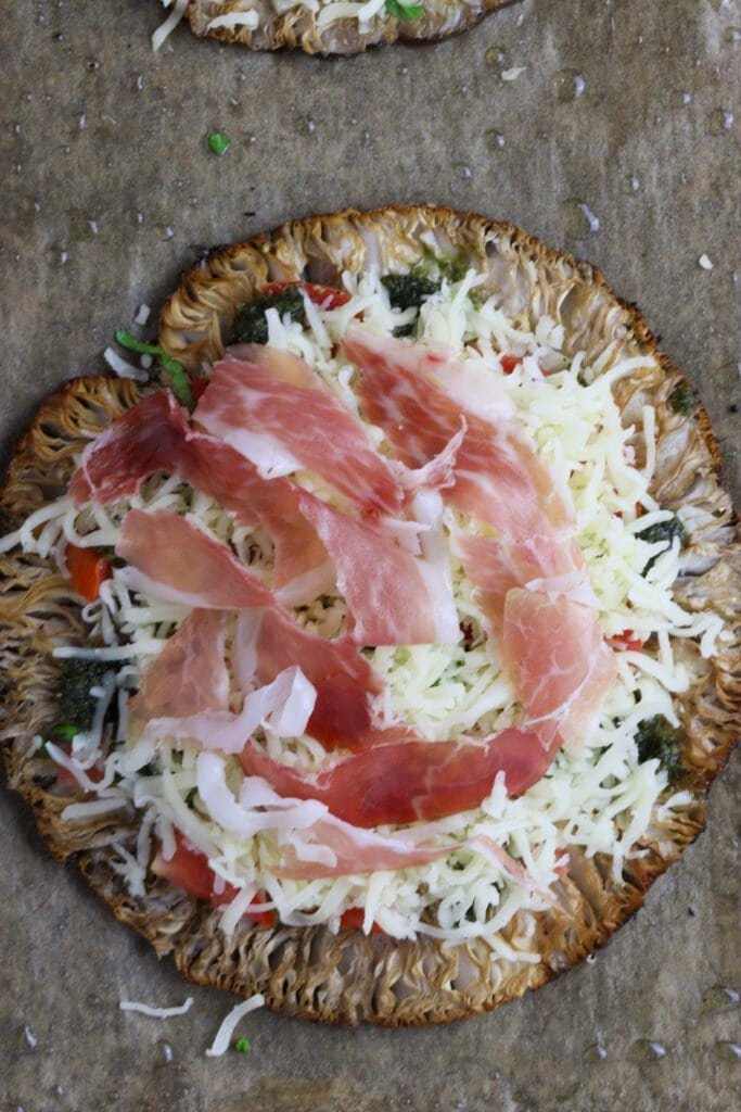 Top view of mushroom pizza just being topped with prosciutto.