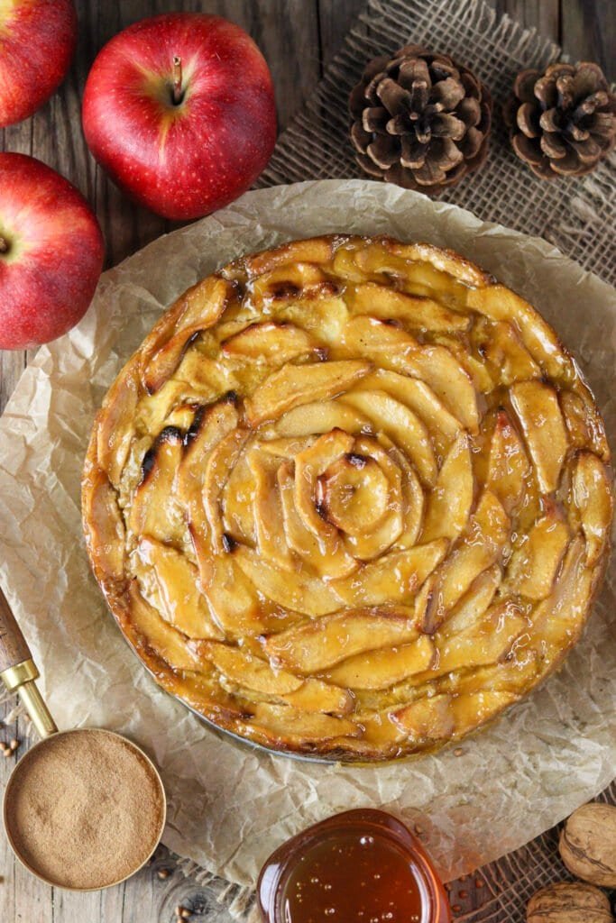 Warm buckwheat cake with apples brushed with warm apricot jam. Apples, cinnamon and a honey jar in the background with two pine cones.