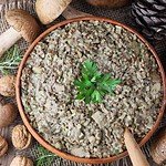 A top view of a rustic handmade bowl of buckwheat with fresh porcini mushrooms and a wooden spoon. Fresh porcini, walnuts and pine cones in the background.
