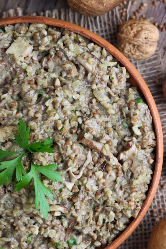 A close view of a bowl of buckwheat with mushrooms, decorated with a parsley sprig on top.