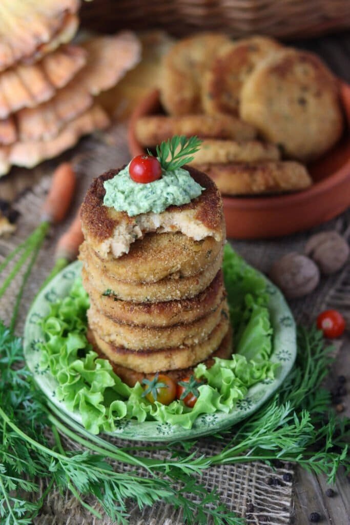 A stack of crispy fried chicken of the woods fritters topped with a small tomato, served with fresh salad and a spoonful of green dip.