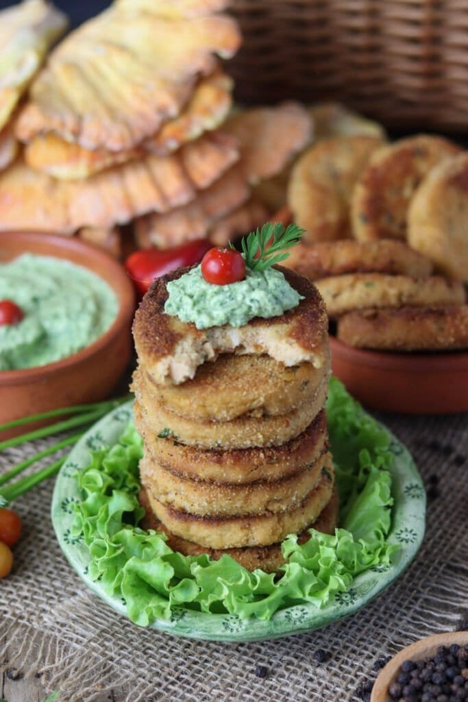 Chicken of the woods mushroom fritters stacked on a small plate with salad, green dip, and a cherry tomato on top.