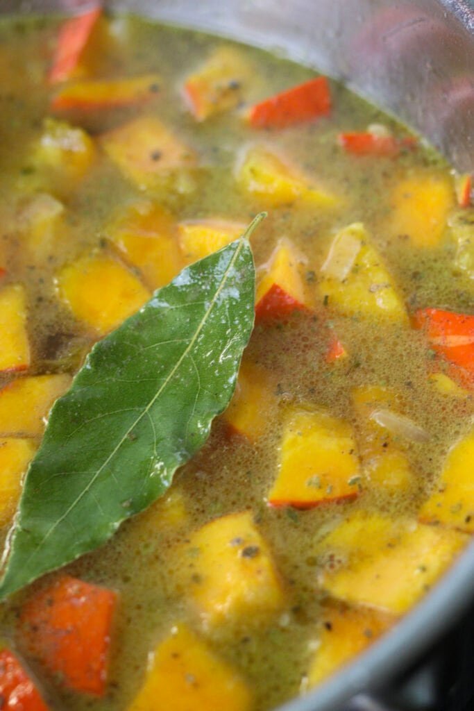 Kuri squash in a pot, cooked, with a bay leaf on top.