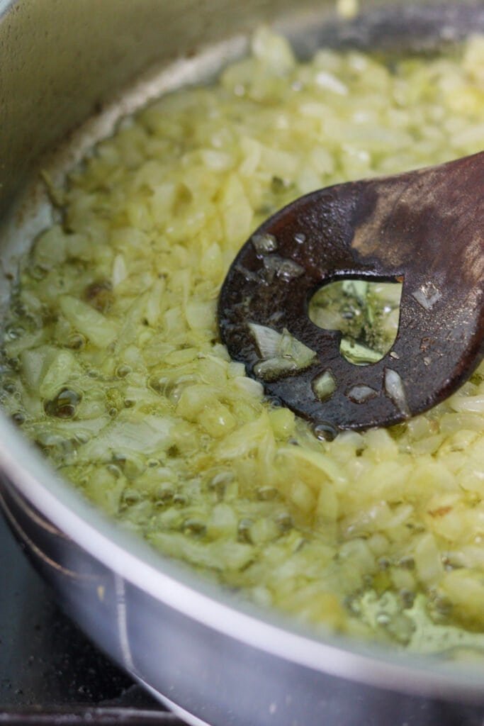 Onions being fried in a pan, until golden brown, with a wooden spoon stiring.