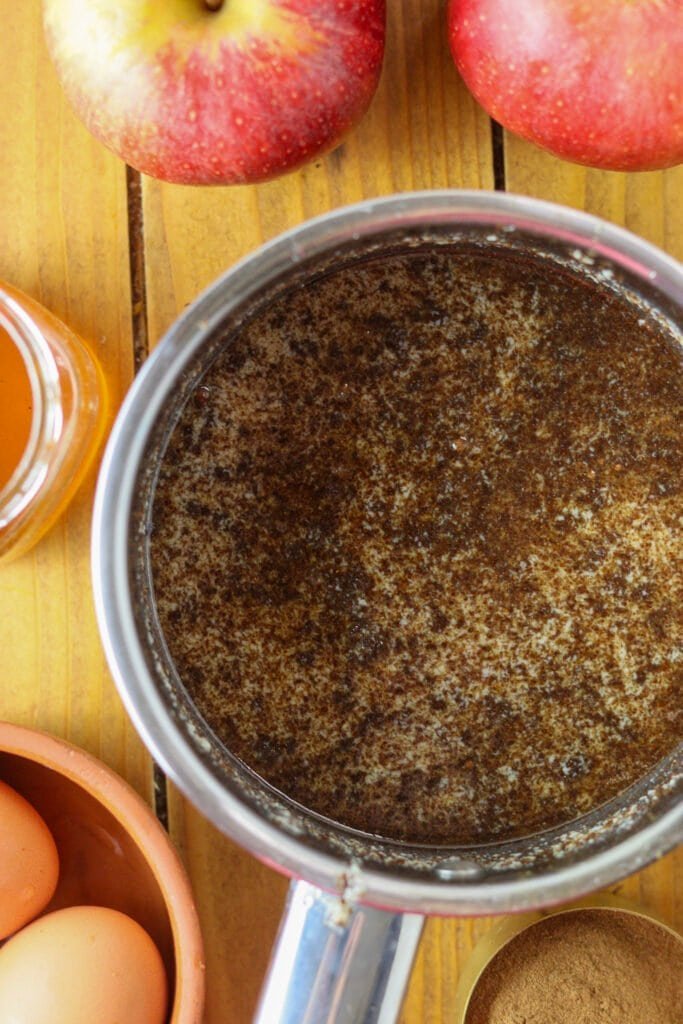 A pot with milk, honey, butter and cinnamon mixture with apples, eggs and honey jar in the background.