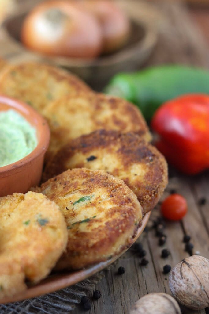 A close view of hot, freshly fried chicken of the woods mushroom fritters on a plate, with green and red pepper in the background.