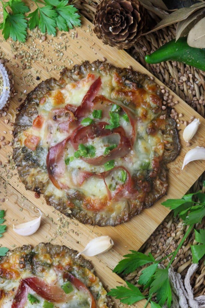 Two parasol mushroom pizzas on a wooden cutting board with garlic cloves and fresh parsley in the background.