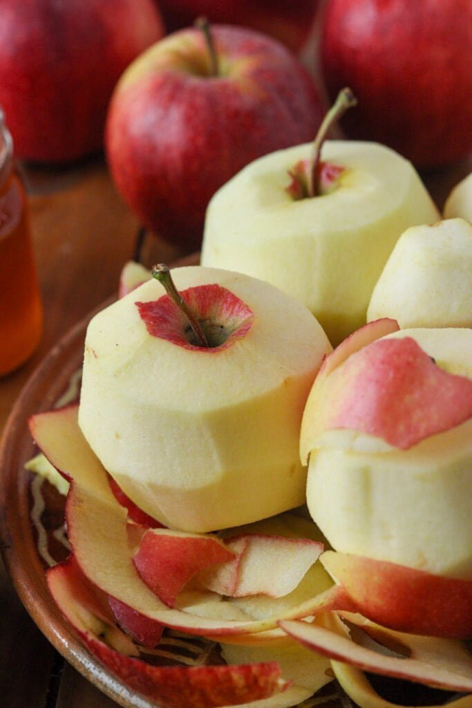 Peeled apples on a rustic plate with whole red apples in the background.