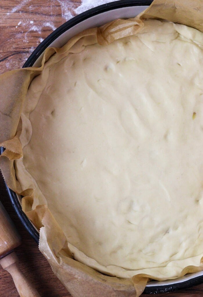 Pizza dough in a large round baking pan, on a piece of brown parchment paper.