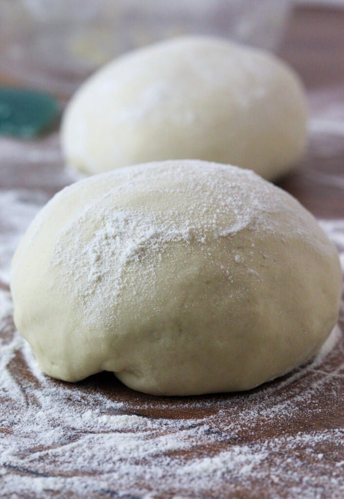 Two pizza dough balls on a floured counter, with flour on top of them.