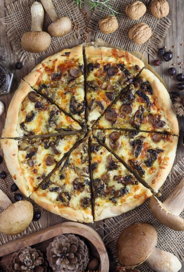 Pizza with porcini on a rustic table, sliced, baked golden brown with porcini mushrooms, walnuts, black pepper and dried rosehip in the background.