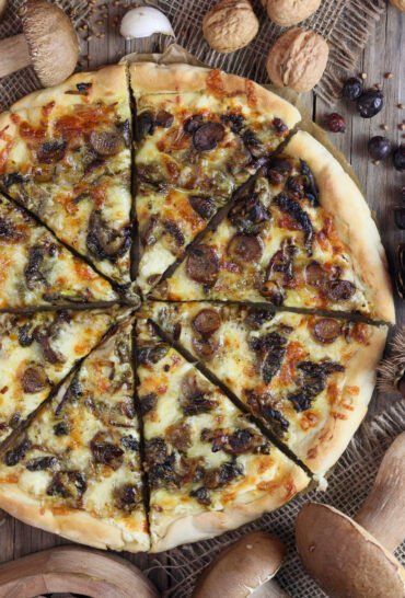 Delicious pizza with porcini recipe with mozzarella, cheddar, sour cream, garlic and oregano. A garlic clove, porcini mushrooms and walnuts in the background,