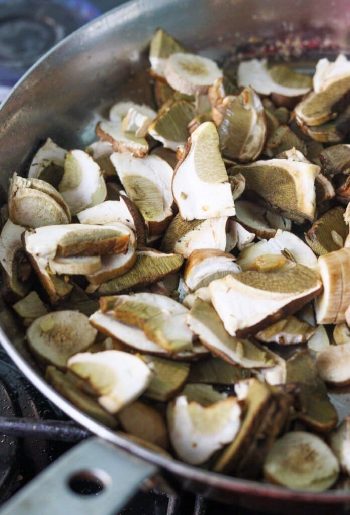 Sliced porcini in a large frying pan on a gas cooking stove.