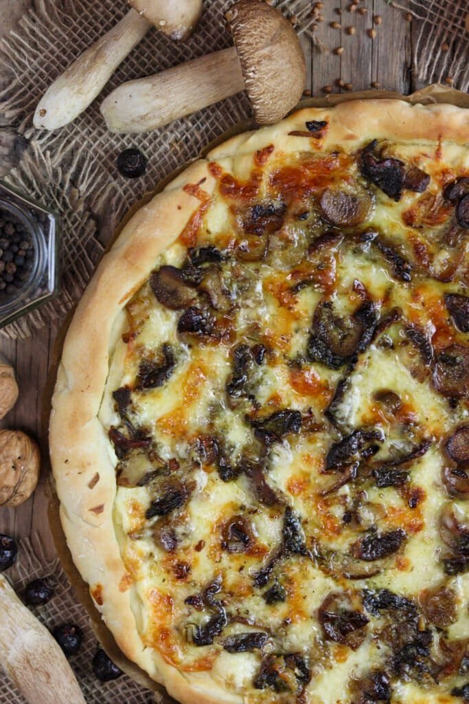 A close view of porcini pizza unsliced, with fresh baby porcini mushrooms and black pepper.