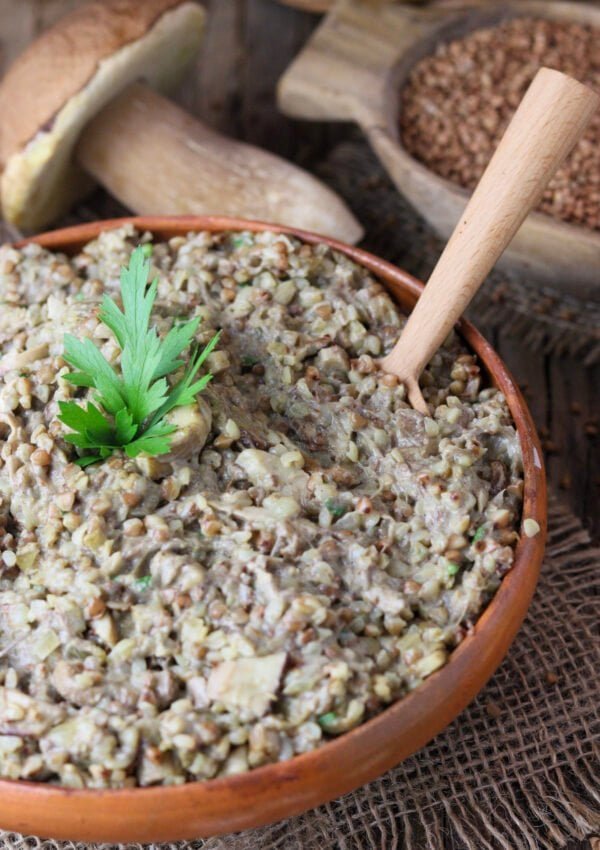 Buckwheat with porcini mushrooms with a wooden bowl of buckwheat groats and one large whole porcini in the background.